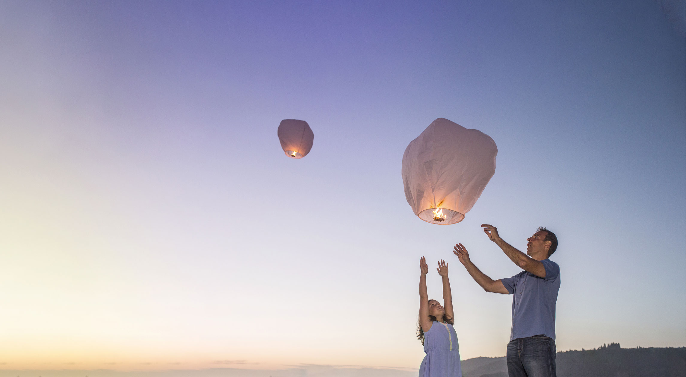 Tyttölapsi ja mies päästävät käsistään itse tehtyjä taivaslyhtyjä.