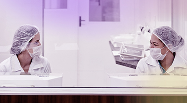 Kaksi laboratoriossa työskentelevää työntekijää istuvat ja keskustelevat keskenään.